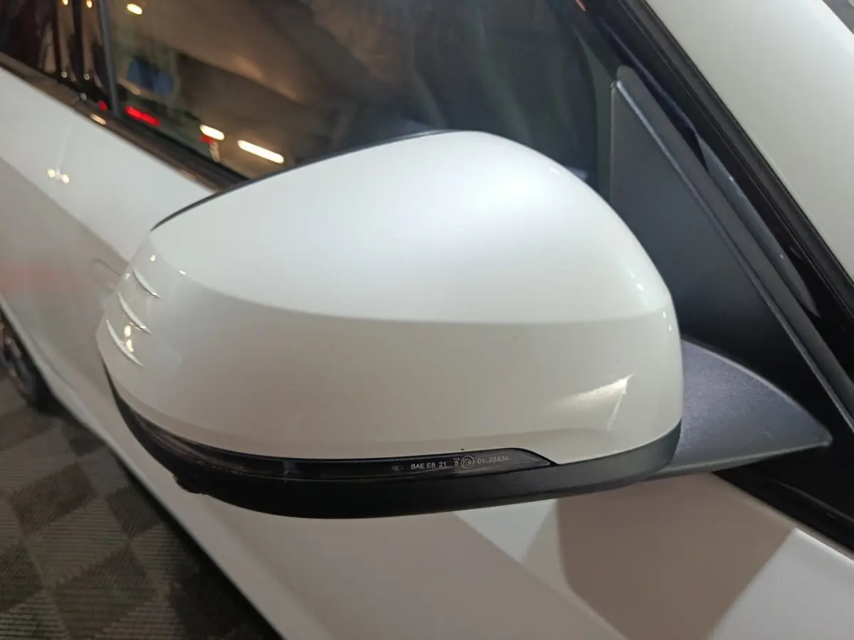 Rétroviseur blanc côté gauche d'une BMW X1 xDrive25e 2024, avec clignotant intégré et carrosserie blanche visible.
