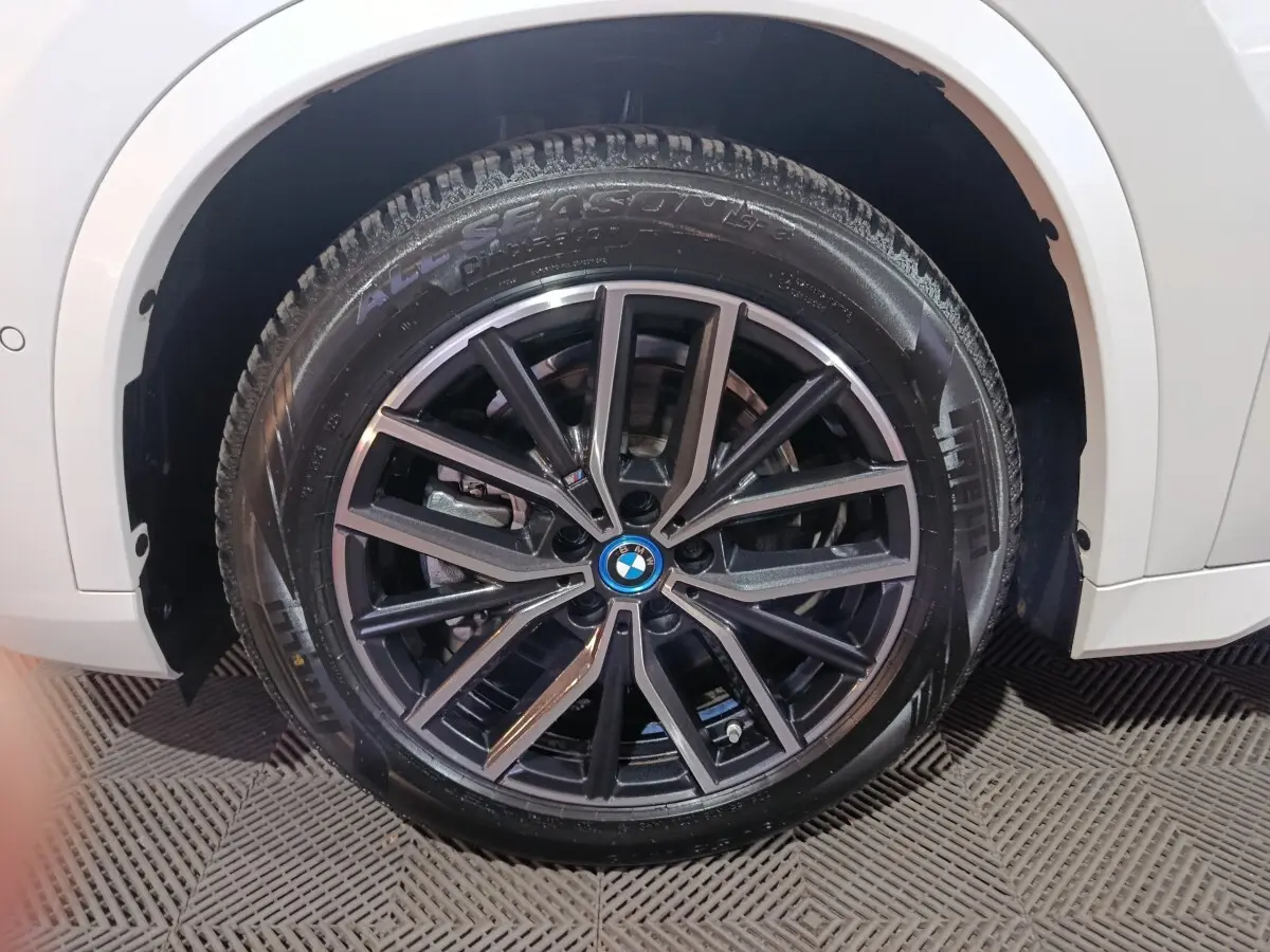 Gros plan sur la roue avant droite noire à jantes alliage du BMW X1 blanc xDrive25e M Sport 2024.