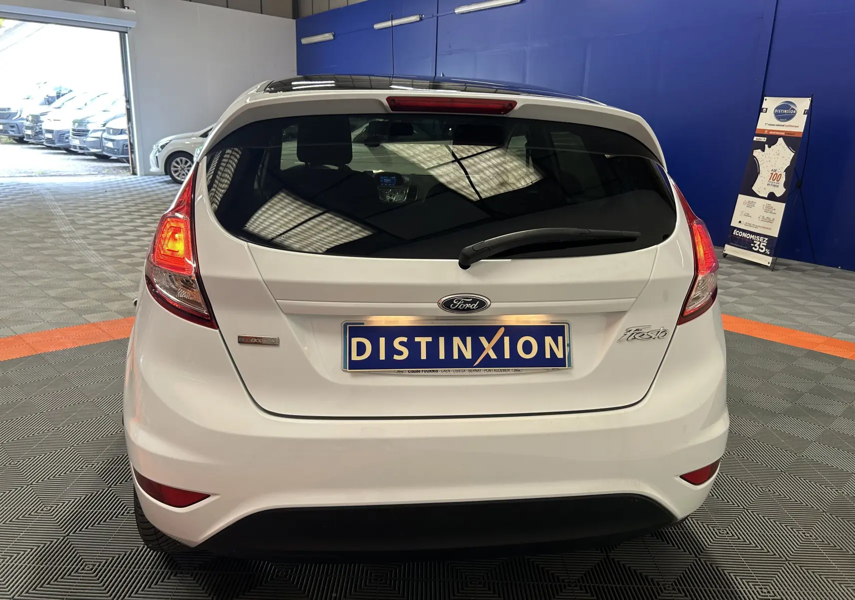 Vue arrière d'une Ford Fiesta blanche avec feux allumés, logo Ford et plaque d'immatriculation Distinxion.