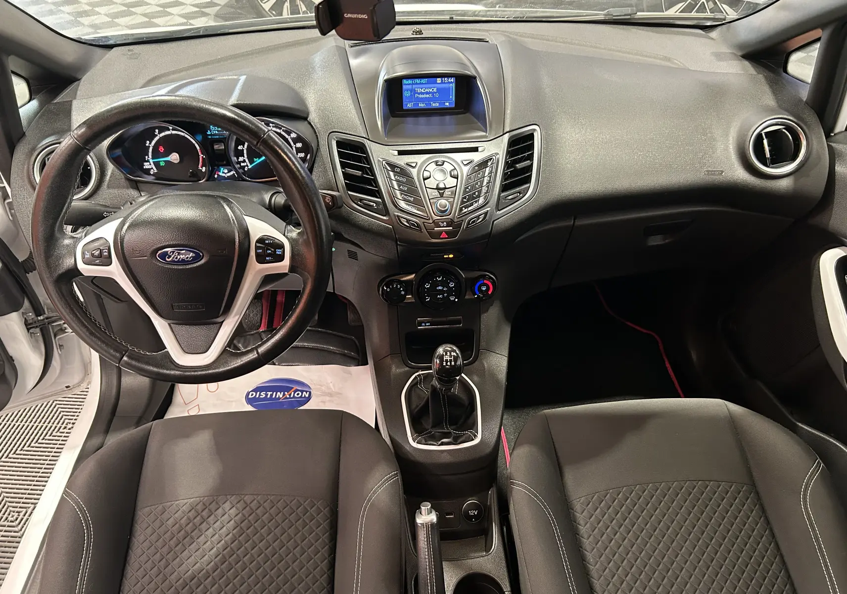 Vue intérieure avant de la Ford Fiesta blanche, montrant le tableau de bord, volant multifonction et levier de vitesse manuel.