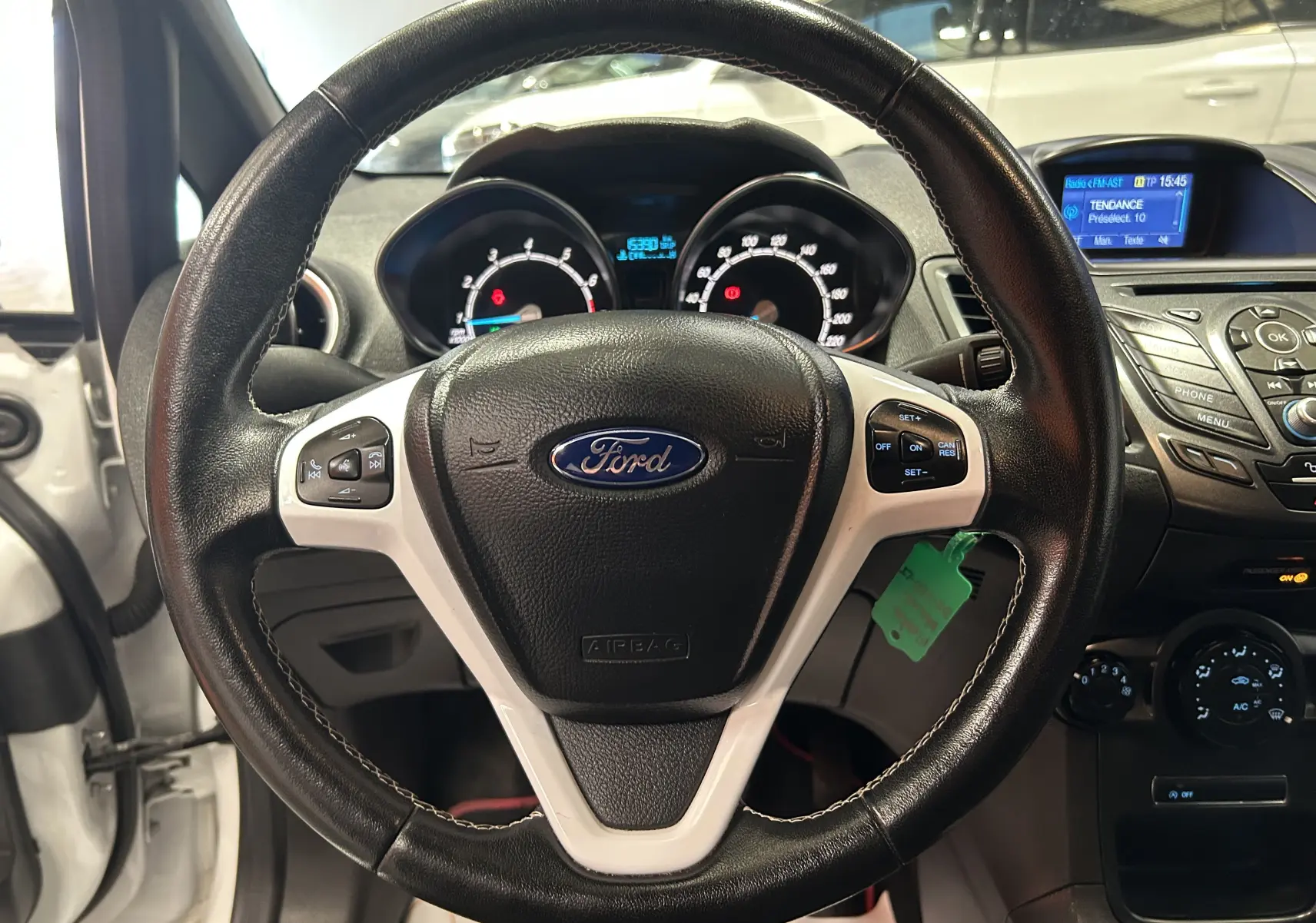 Vue rapprochée du volant en cuir noir avec commandes intégrées d’une Ford Fiesta blanche de 2015, tableau de bord visible.