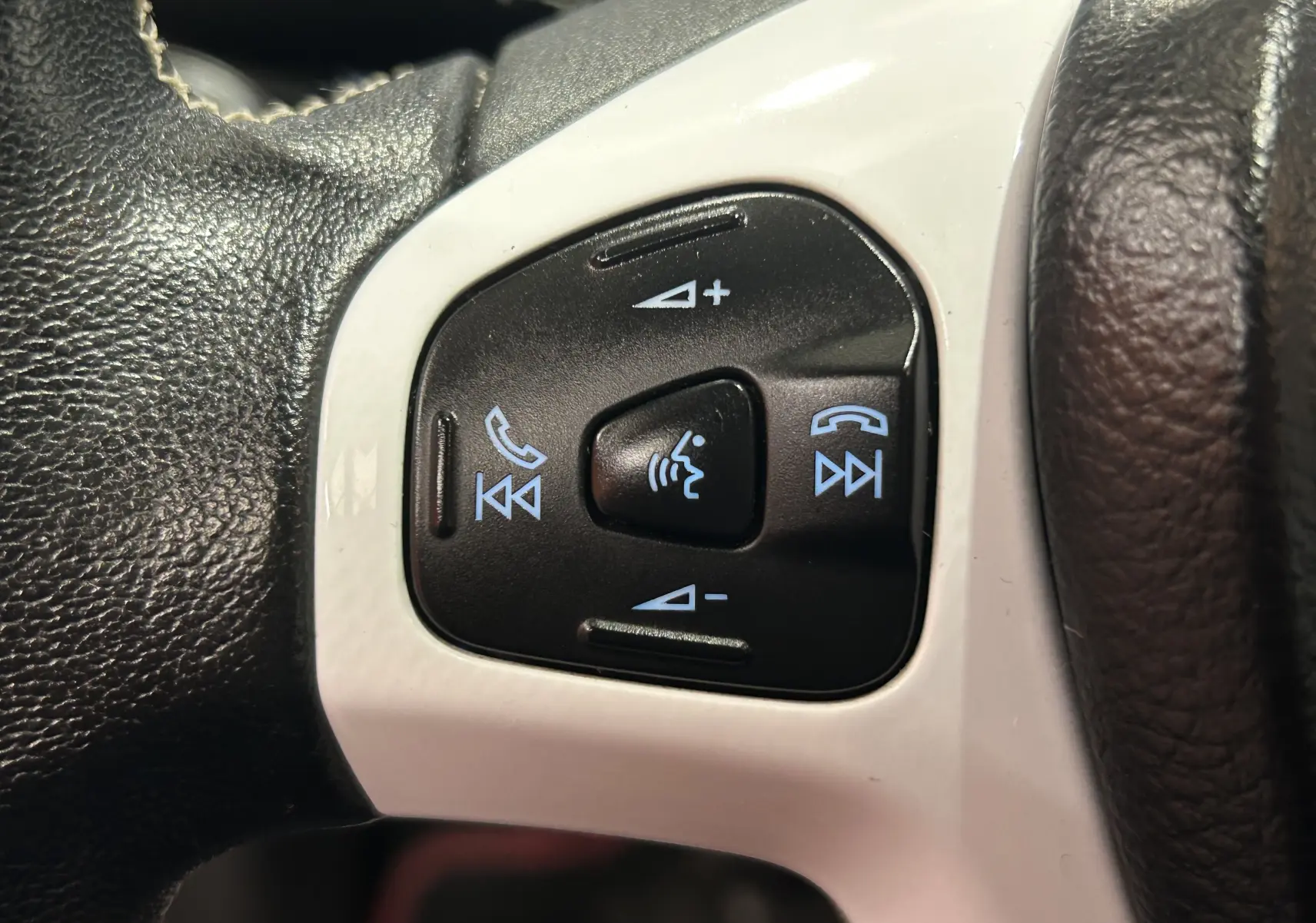 Gros plan sur les commandes noires du volant blanc de la Ford Fiesta EcoBoost 2015, avec boutons de volume et téléphone.