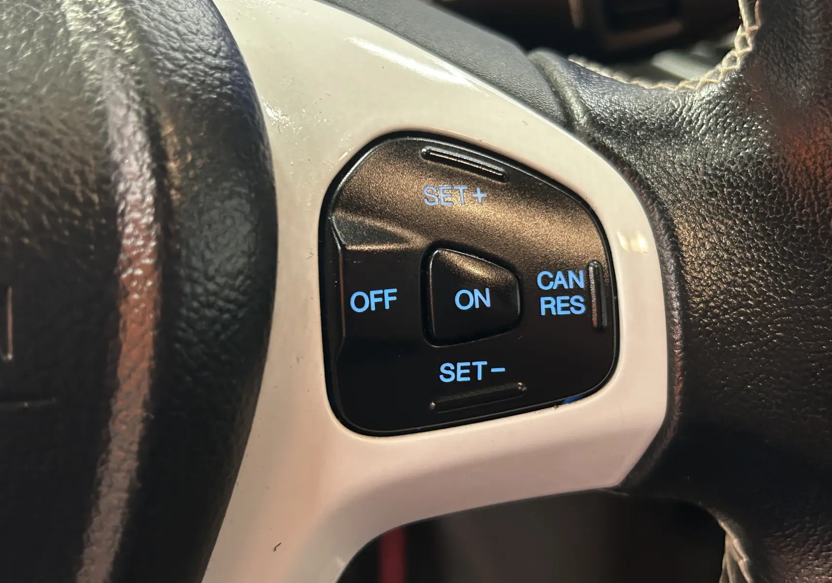 Gros plan sur les commandes de régulateur de vitesse à droite du volant noir avec insert blanc d'une Ford Fiesta blanche de 2015.