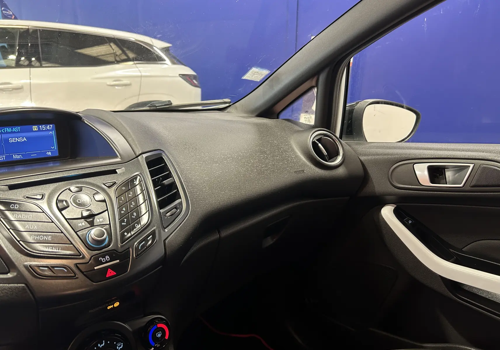 Vue intérieure côté passager de la Ford Fiesta blanche, mettant en valeur le tableau de bord et la console centrale noire.
