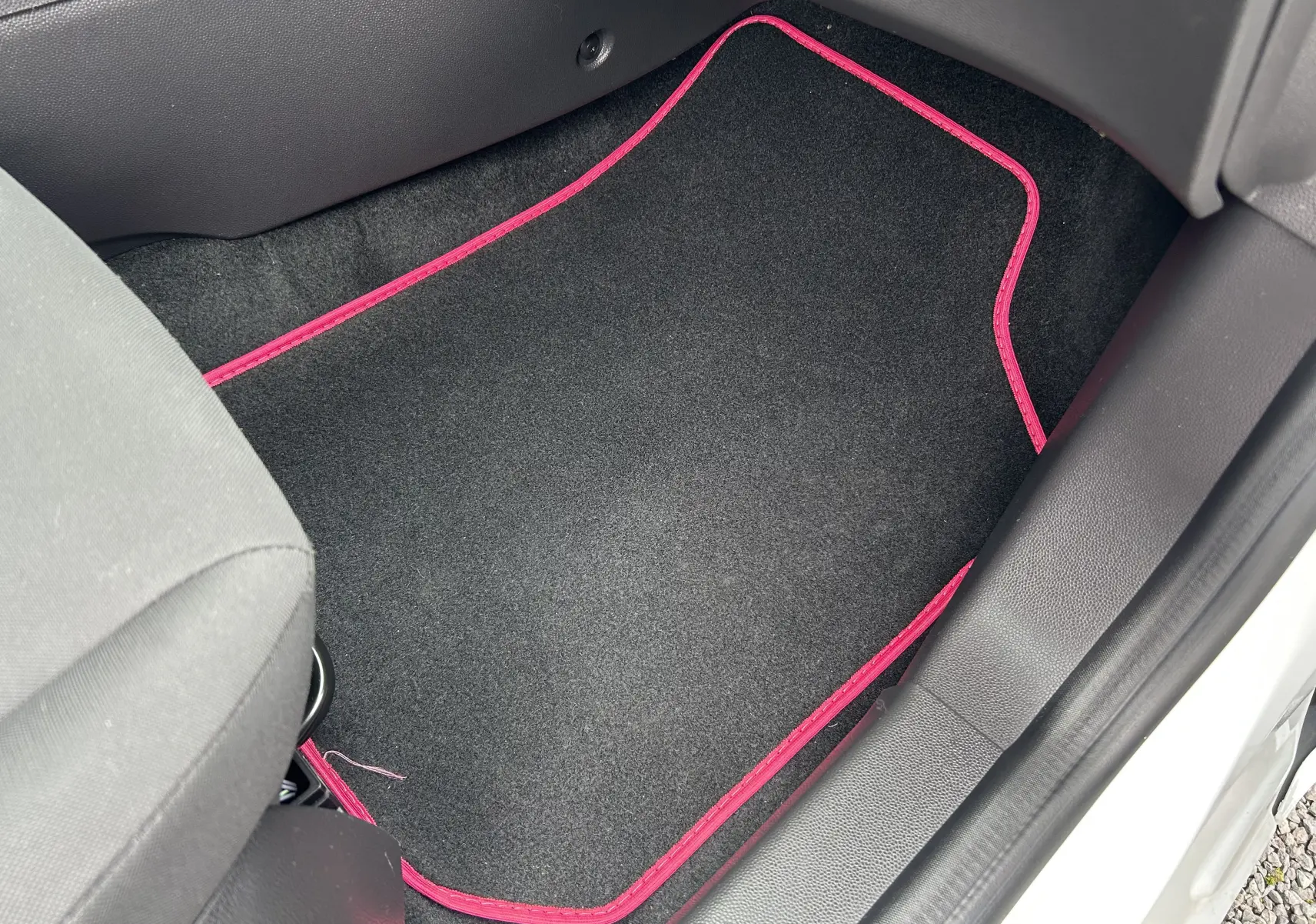 Vue intérieure côté passager avant d'une Ford Fiesta blanche de 2015, avec tapis de sol noir bordé de rose.