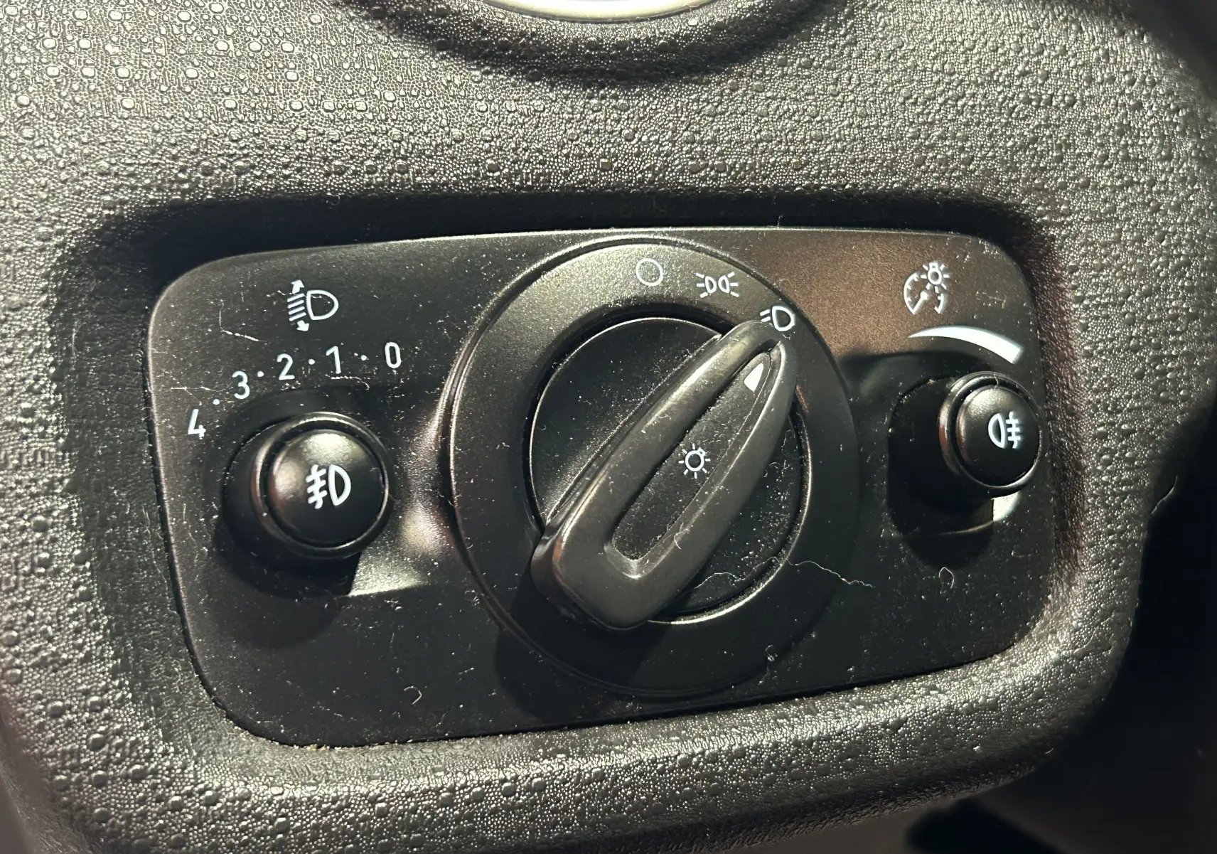Gros plan sur le bouton de commande des phares et feux antibrouillard du tableau de bord d'une Ford Fiesta blanche.