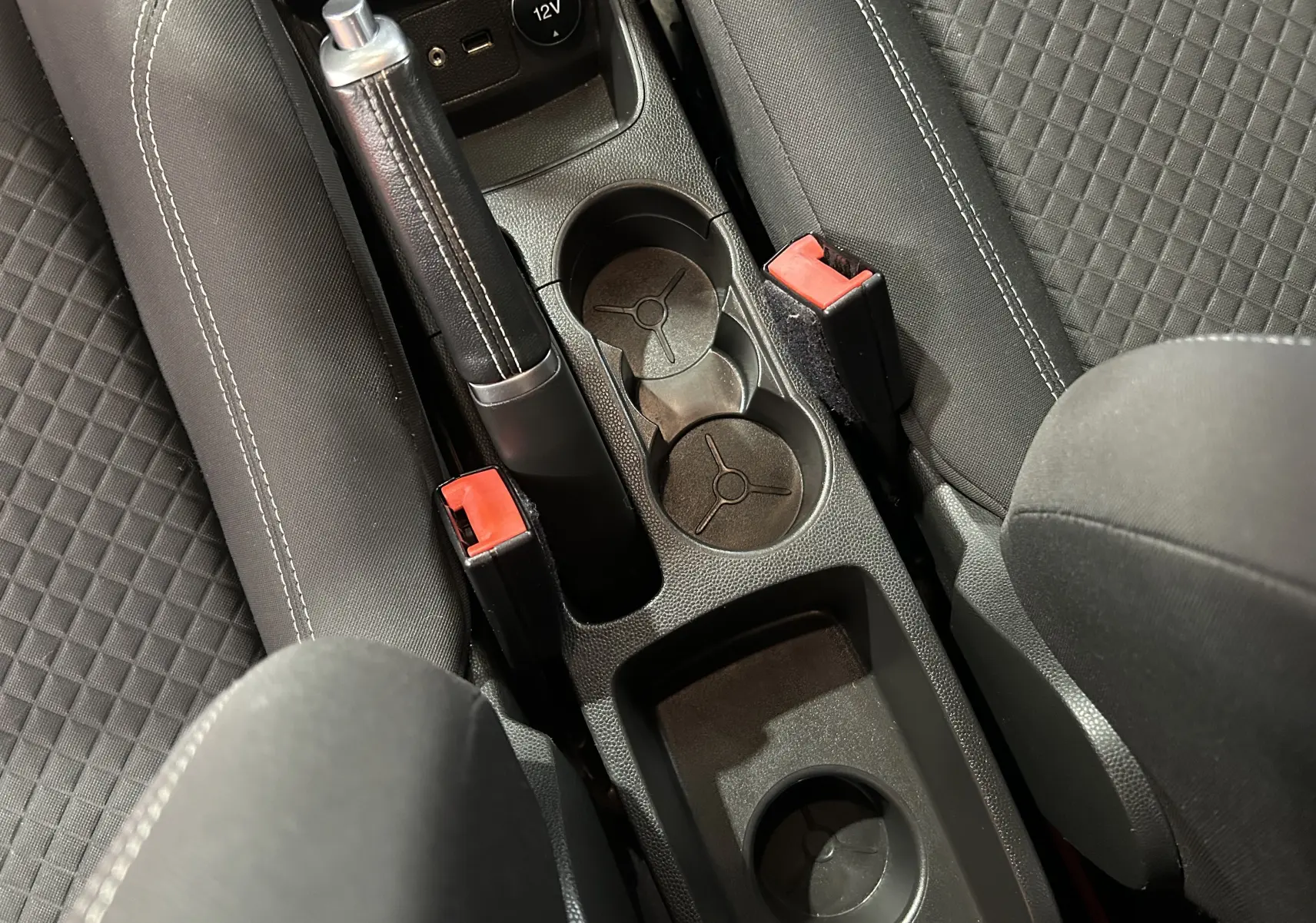 Vue plongeante sur la console centrale noire avec frein à main, porte-gobelets et sièges tissu gris de la Ford Fiesta 2015.