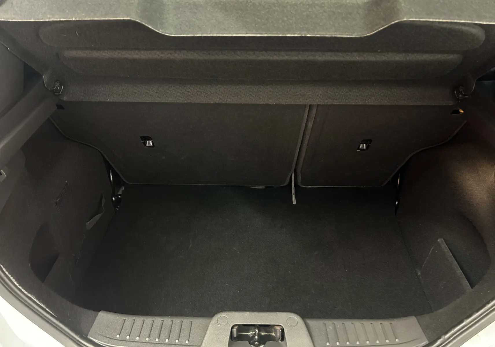 Coffre ouvert vu de l'arrière d'une Ford Fiesta blanche, montrant un espace de chargement propre et vide.