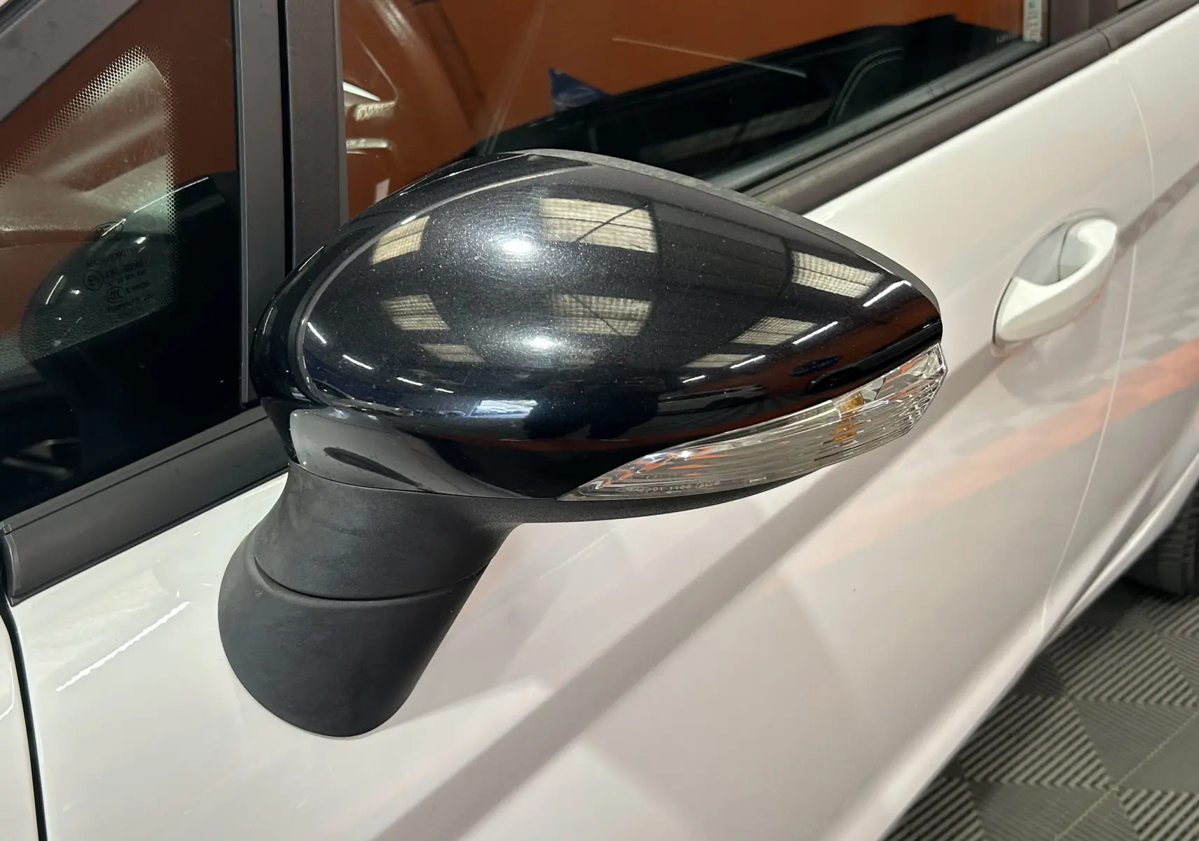 Gros plan sur le rétroviseur noir côté gauche d'une Ford Fiesta blanche, avec clignotant intégré visible.
