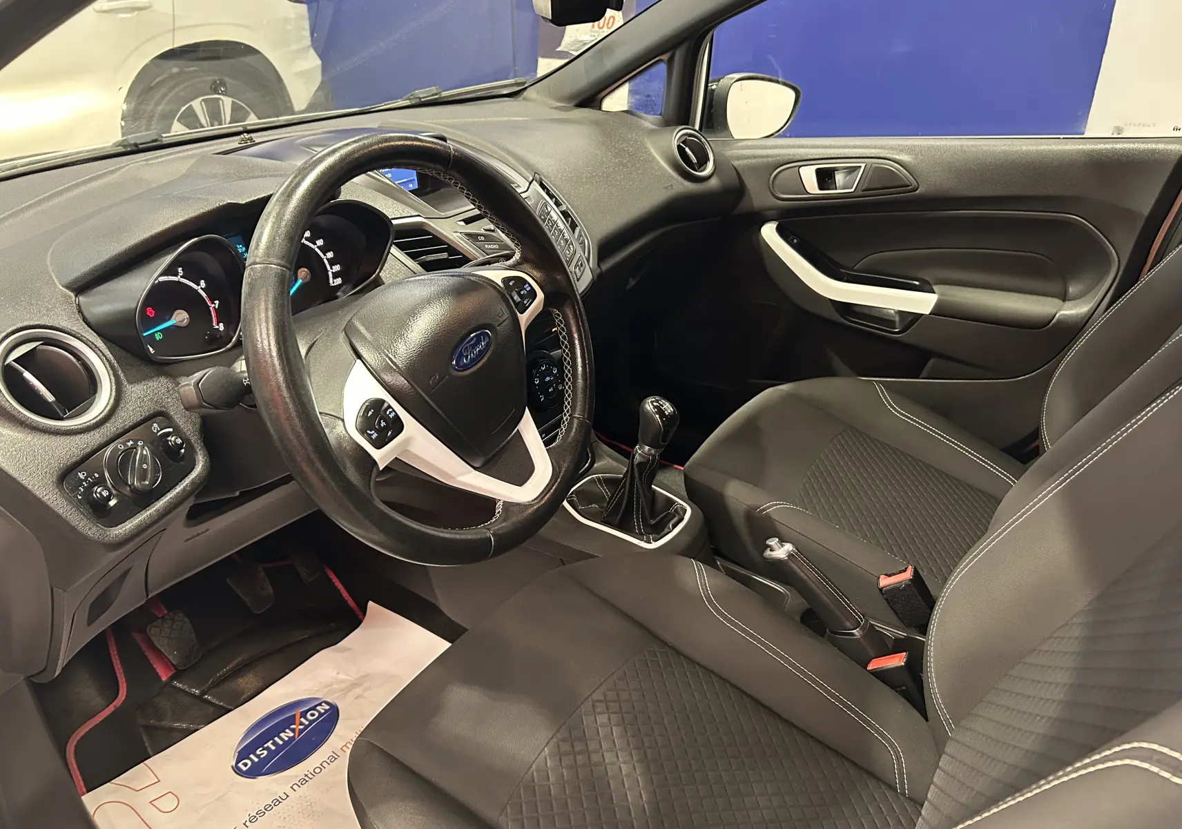 Vue intérieure côté conducteur de la Ford Fiesta 2015 avec volant multifonction et sellerie tissu noire.
