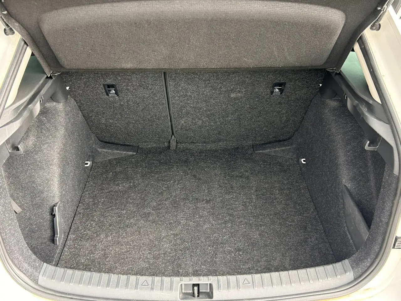 Coffre ouvert vu de l'arrière d'une Skoda Scala TSI 116 DSG7 blanc Candy, espace de rangement vide et tapissé gris.