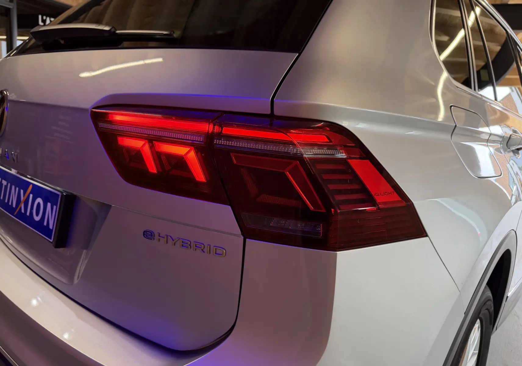 Vue arrière droite d'un Volkswagen Tiguan gris clair 1.4 e-Hybrid 2022 avec feux arrière allumés et logo e-Hybrid visible.