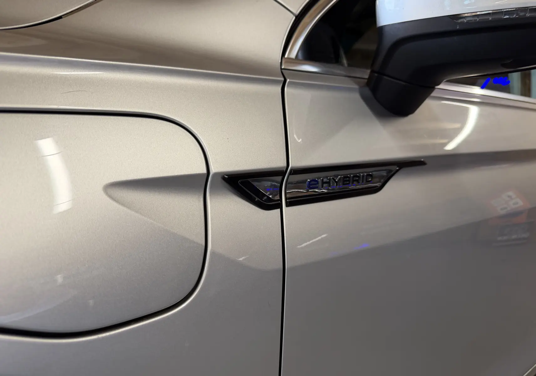 Gros plan sur la trappe de recharge côté gauche du Volkswagen Tiguan gris clair avec logo e-HYBRID brillant.