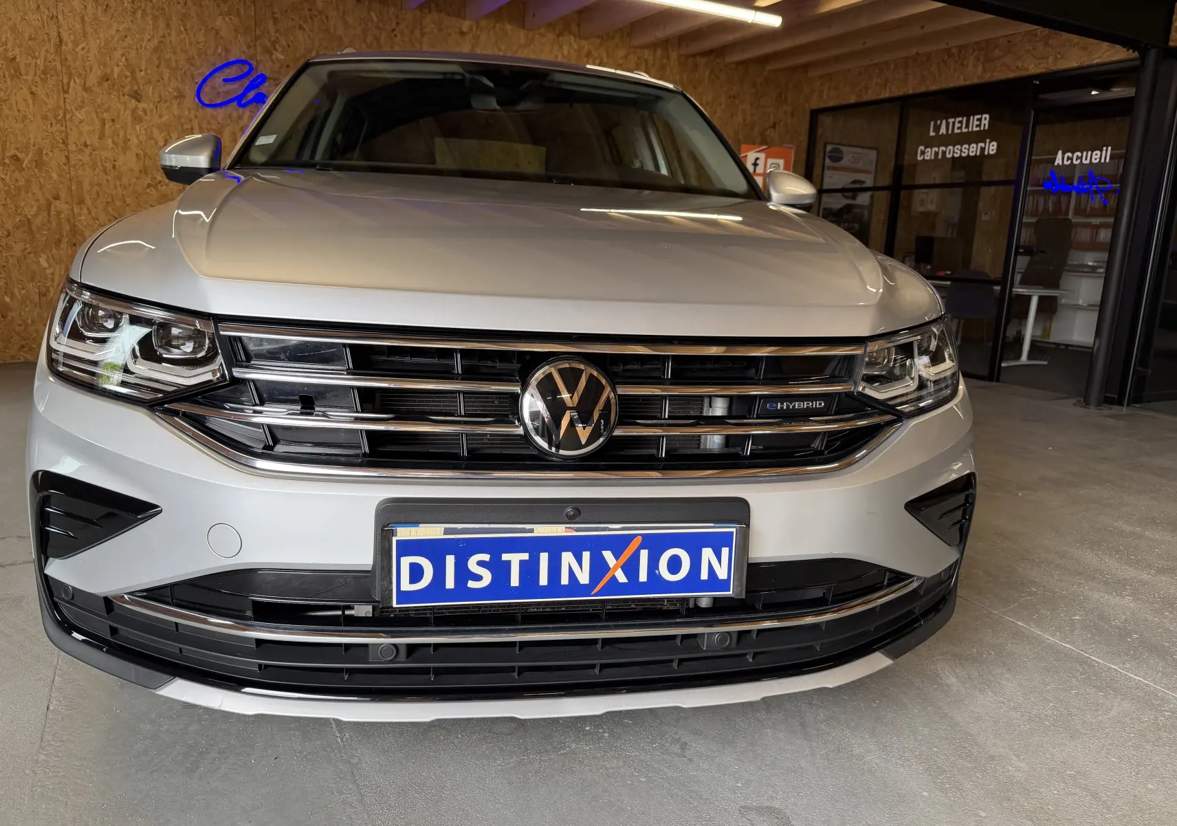 Volkswagen Tiguan gris clair en 3/4 avant droit, hybride rechargeable, avec calandre et phares LED visibles en intérieur.