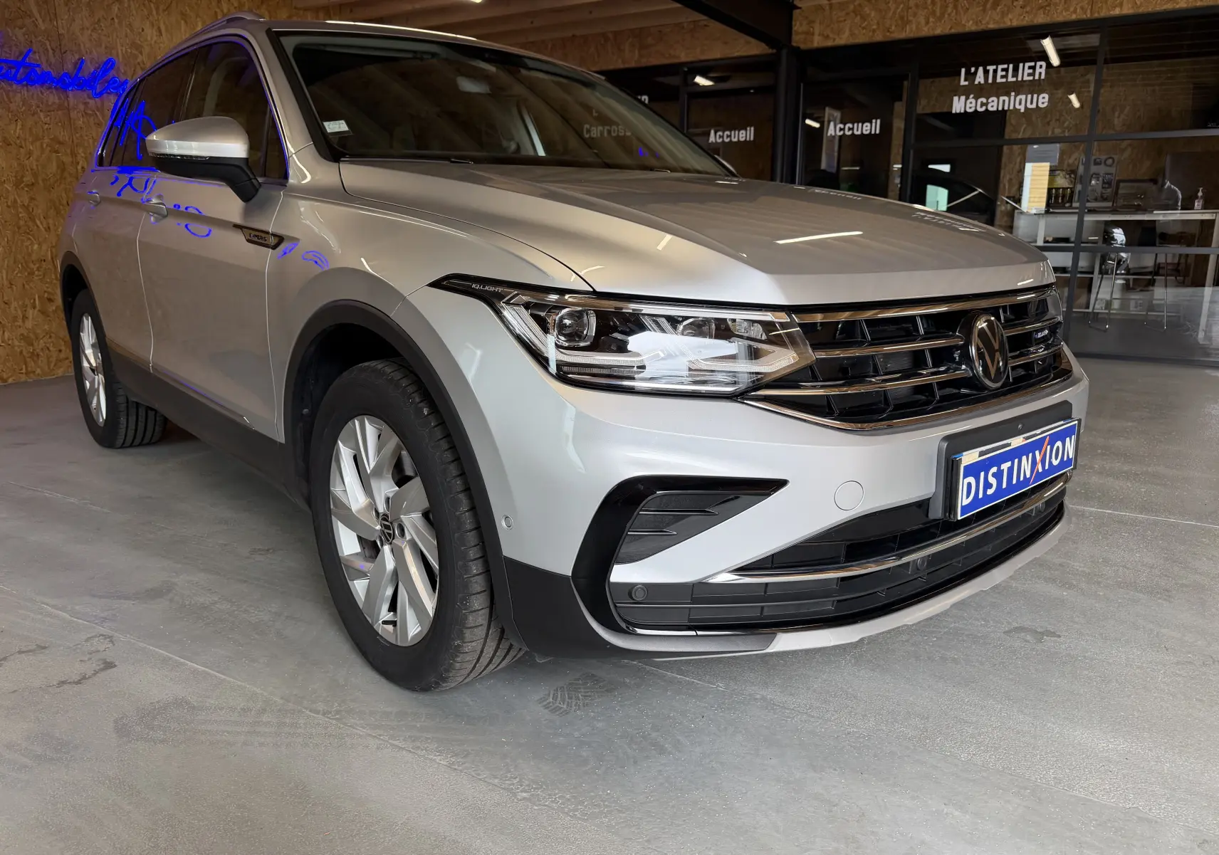Vue 3/4 avant droite d'un Volkswagen Tiguan gris clair 2022, hybride rechargeable, avec calandre noire et jantes alliage.