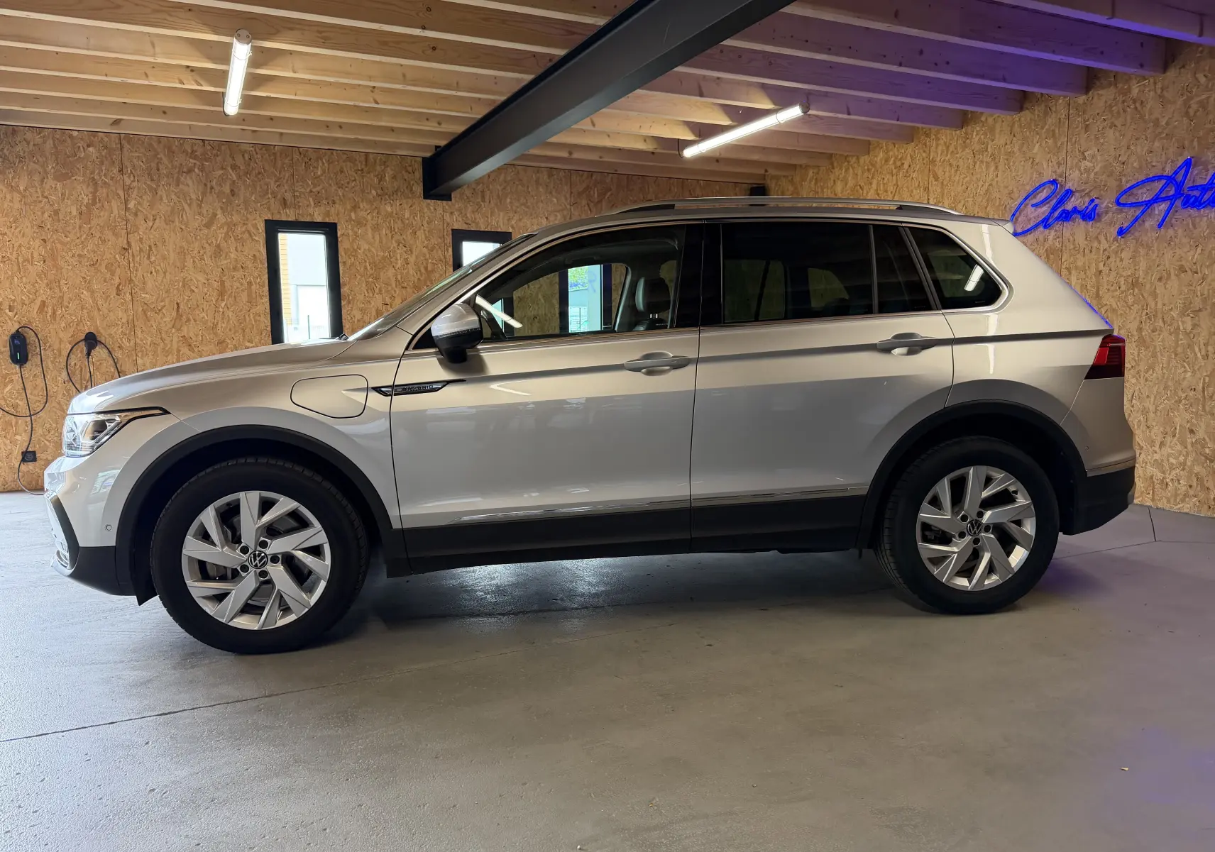 Vue de profil côté gauche d'un Volkswagen Tiguan 1.4 e-Hybrid gris clair, avec prises de recharge visibles sur l'aile avant.