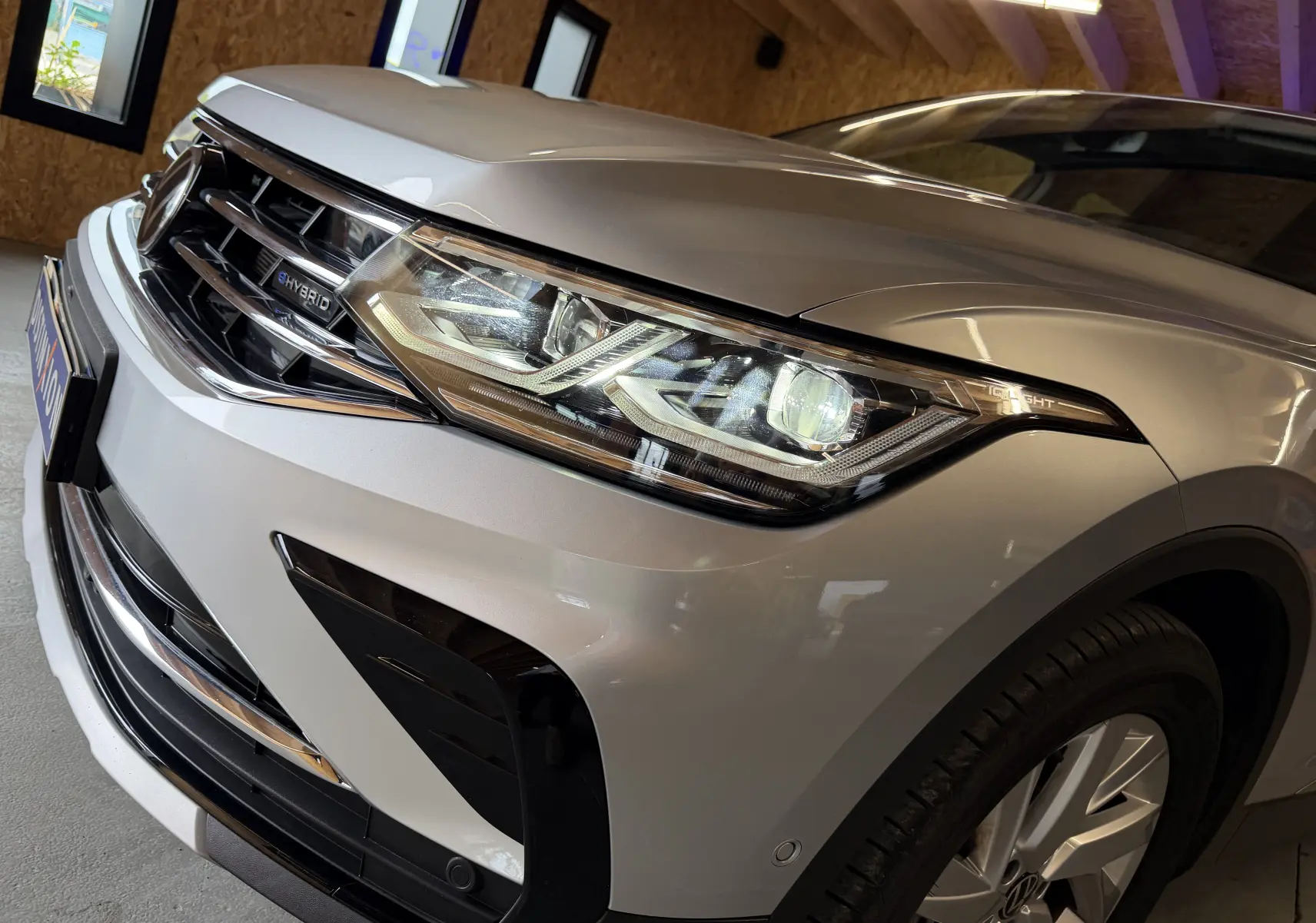 Vue rapprochée 3/4 avant droit du Volkswagen Tiguan gris clair hybride rechargeable, mettant en valeur le phare LED et la calandre.