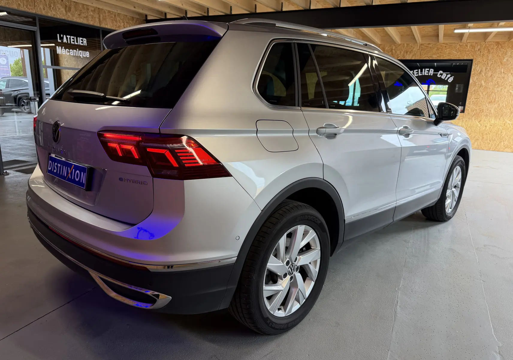 Vue 3/4 arrière droite d'un Volkswagen Tiguan gris clair hybride rechargeable avec feux arrière LED allumés en intérieur d'atelier.