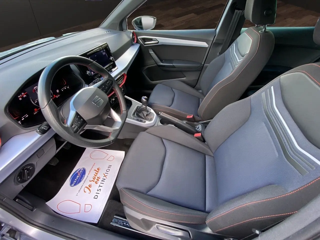 Intérieur avant droit du SEAT Arona 2024 avec sièges tissu noirs à surpiqûres rouges et tableau de bord digital.