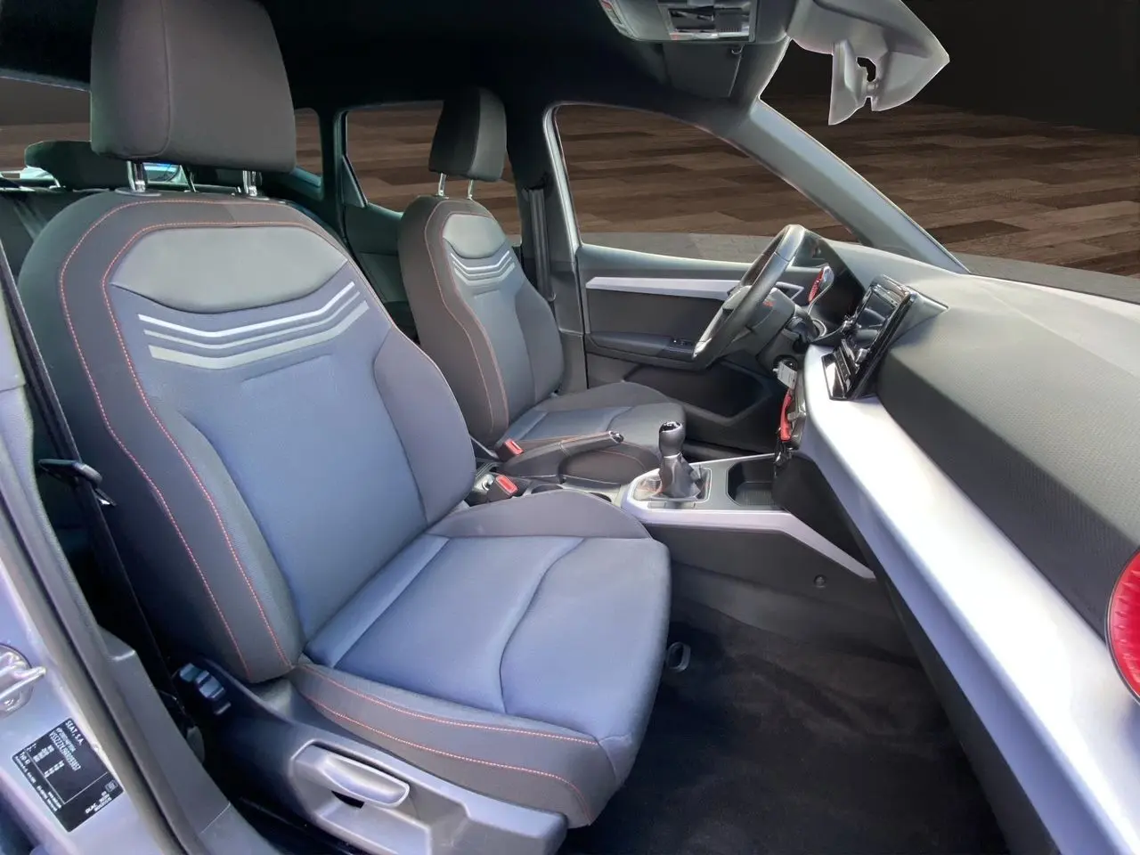Intérieur avant du SEAT Arona 2024, vue côté gauche, sièges tissu noir avec surpiqûres rouges et tableau de bord moderne.