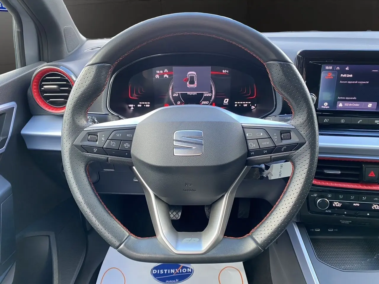 Volant perforé avec surpiqûres rouges et tableau de bord digital d'une SEAT Arona gris silver intérieur noir, vue de face.