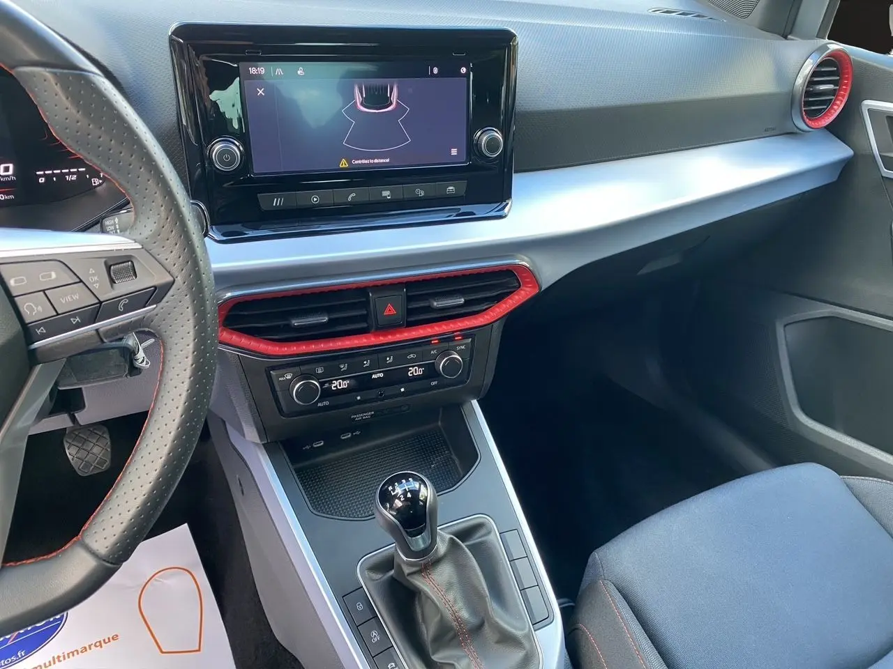 Vue intérieure du tableau de bord et console centrale d'une SEAT Arona 2024 avec boîte manuelle, garnitures noires et touches rouges.