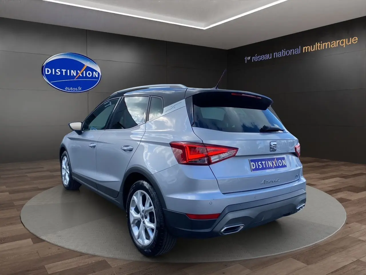 Vue 3/4 arrière droite d'un SEAT Arona gris silver avec toit noir et jantes alu 17 pouces dans un showroom.