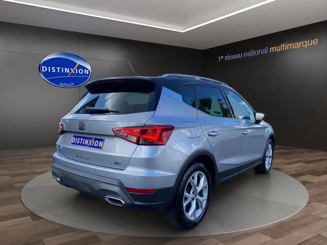 Vue 3/4 arrière droite d'un SEAT Arona gris silver avec toit noir et jantes alu 17 pouces dans un showroom.