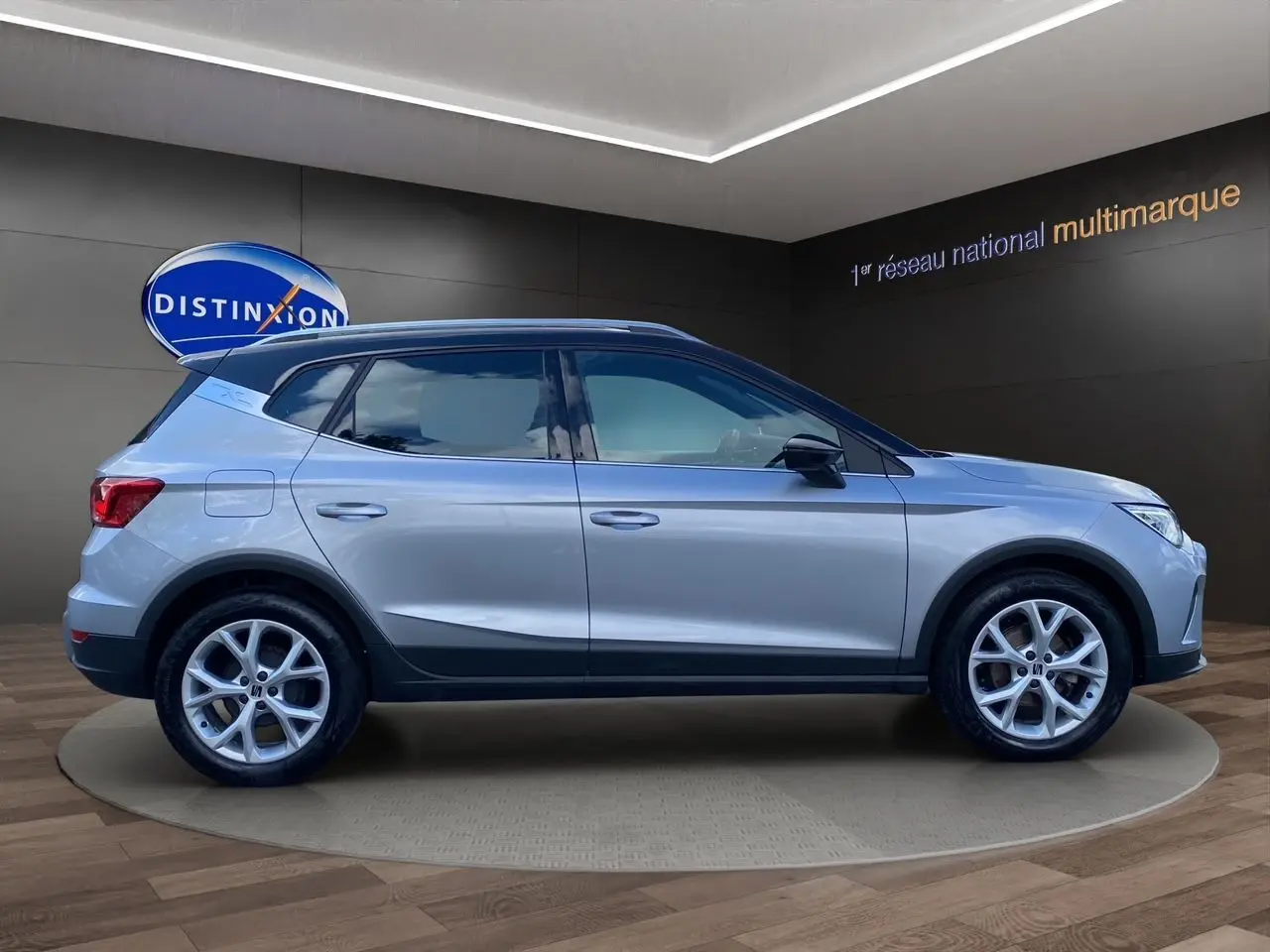 Vue de profil côté gauche du SEAT Arona gris silver avec toit noir et jantes alu 17 pouces en intérieur showroom.