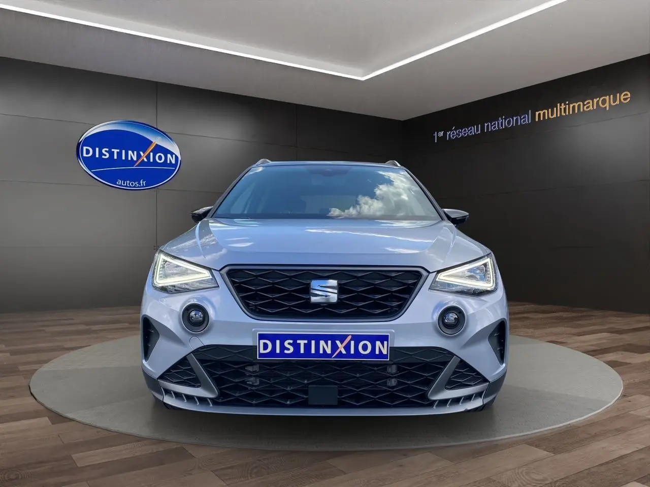 Vue frontale d'un SEAT Arona gris silver avec toit noir, feux LED allumés et calandre noire en showroom.