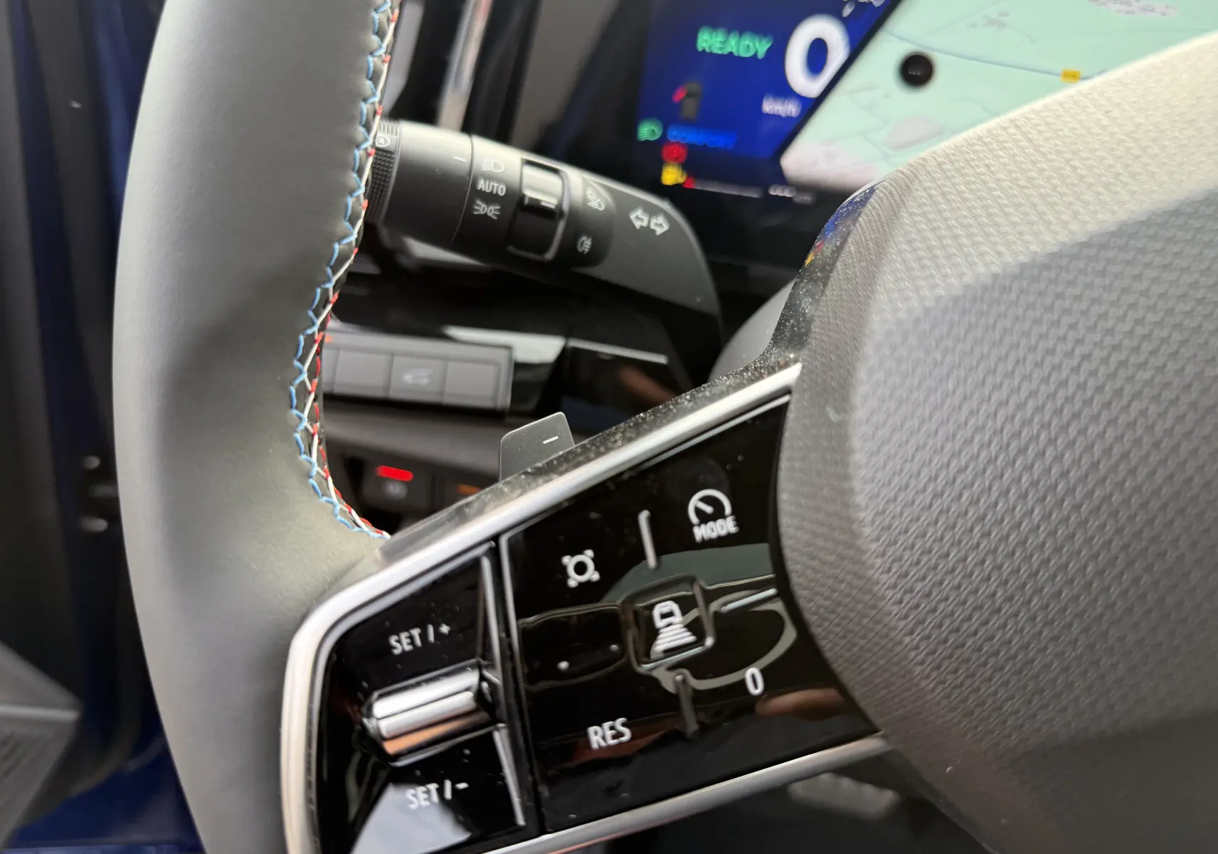 Gros plan sur le volant cuir avec surpiqûres tricolores du Renault Austral 2025 bleu iron, affichage numérique en arrière-plan.