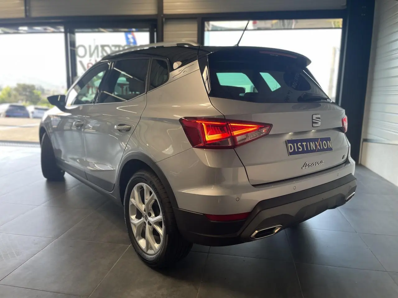 Vue 3/4 arrière droite d'un SEAT Arona 2024 rouge passion avec feux arrière allumés en showroom.