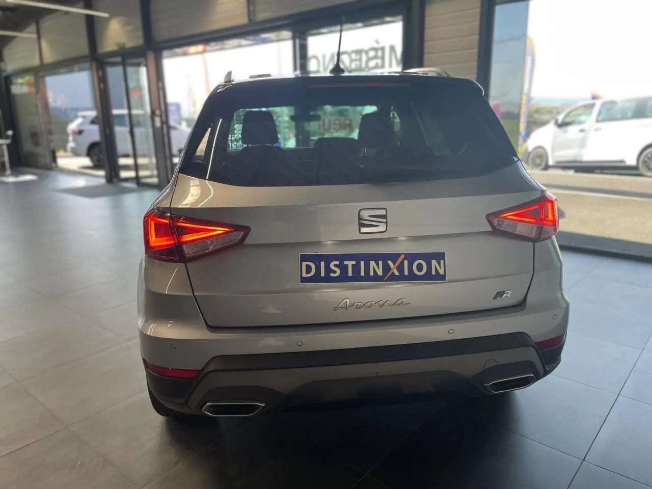 Vue arrière d'un SEAT Arona gris GRS 2024 avec feux allumés et logo FR dans un showroom lumineux.