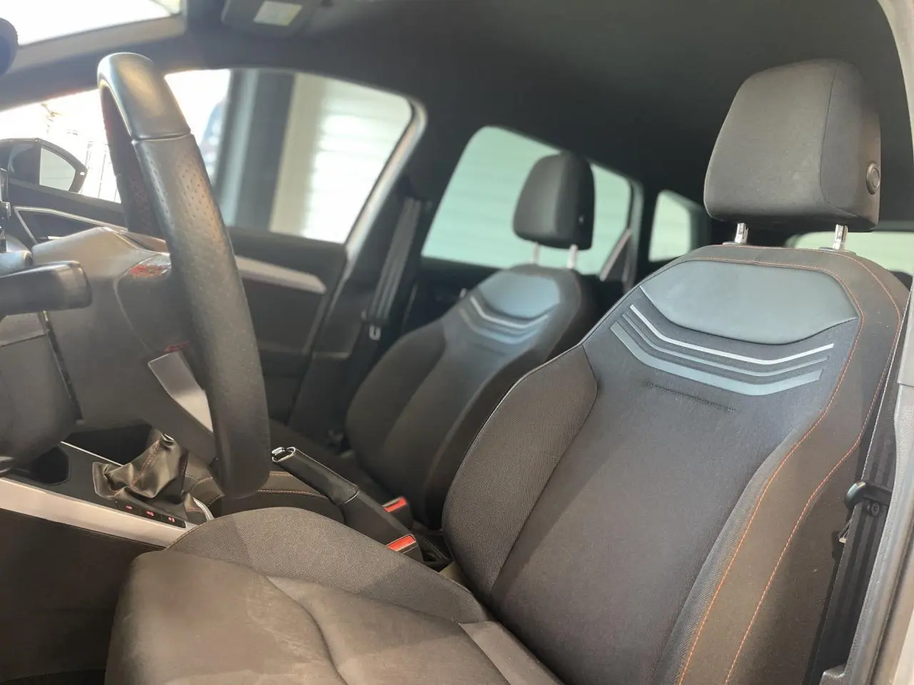 Vue intérieure côté conducteur du SEAT ARONA 2024 avec sièges textile noirs et volant sport cuir à méplat.