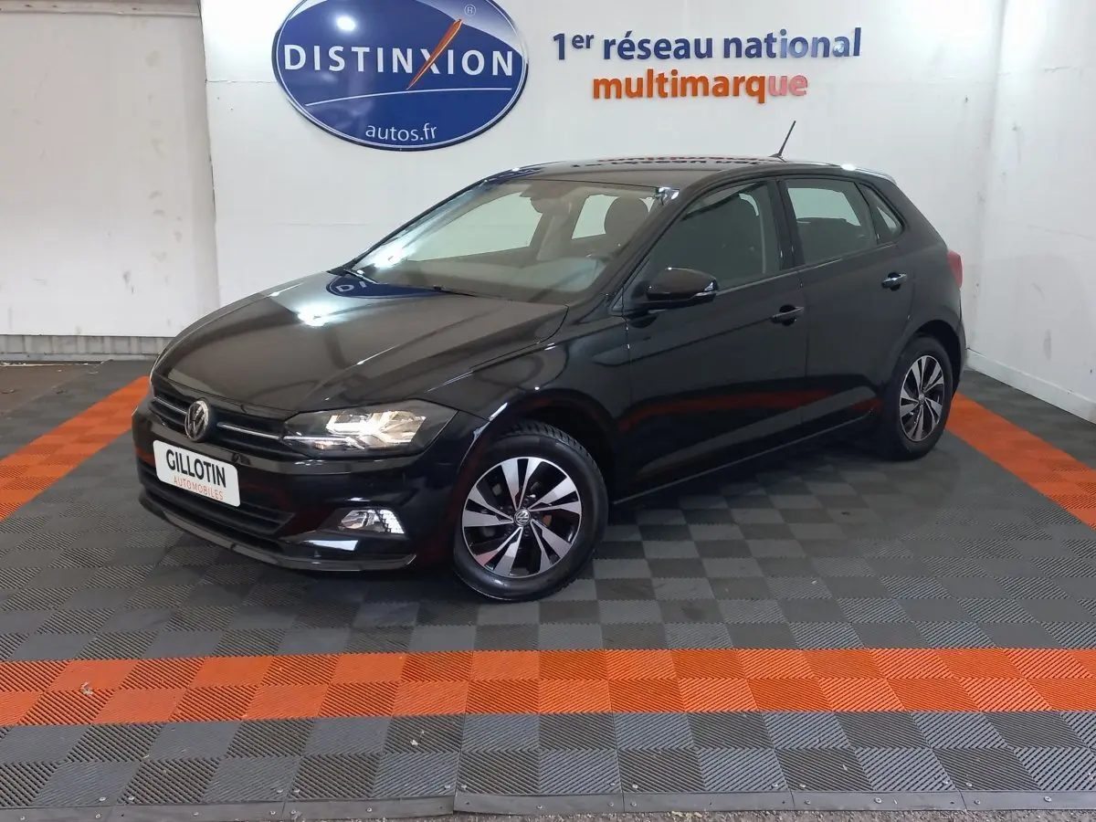 Volkswagen Polo noire vue en 3/4 avant droit dans un showroom avec sol gris et bandes orange.