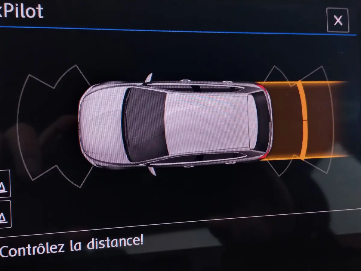 Vue de dessus d'une Volkswagen Polo blanche sur l'écran de stationnement avec alertes de proximité arrière en orange.