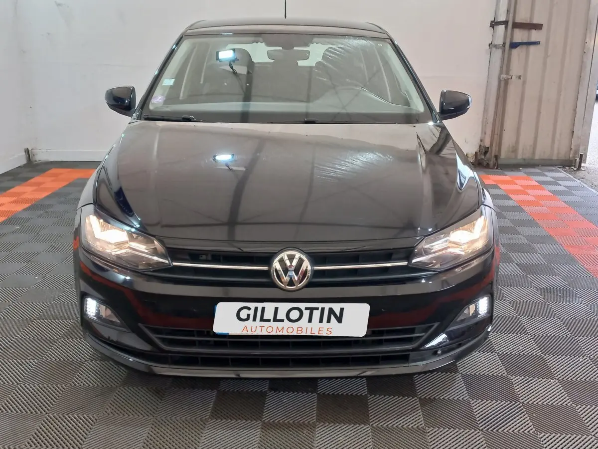 Vue frontale d'une Volkswagen Polo noire 2020 avec phares et feux diurnes allumés en intérieur showroom.