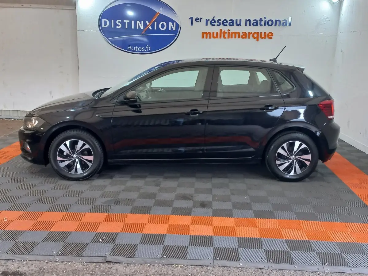 Profil côté gauche d'une Volkswagen Polo noire 2020 stationnée en intérieur sur un sol à damiers gris et orange.