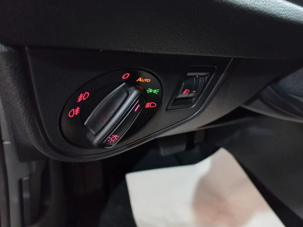 Gros plan sur le bouton de commande des phares avec réglage automatique dans l'habitacle noir du Volkswagen Polo 2020.