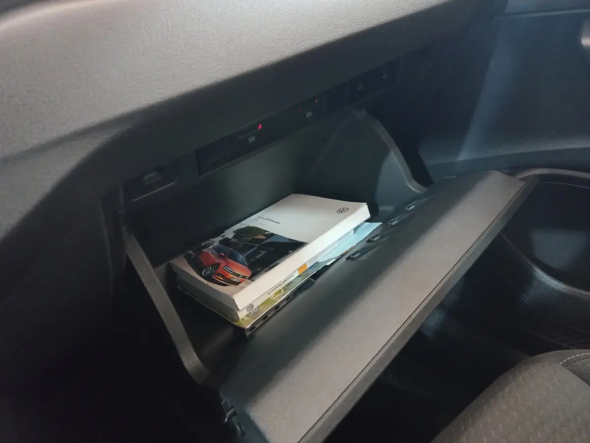 Vue intérieure du coffre à gants ouvert de la Volkswagen Polo noire, avec manuel et documents visibles à l'intérieur.