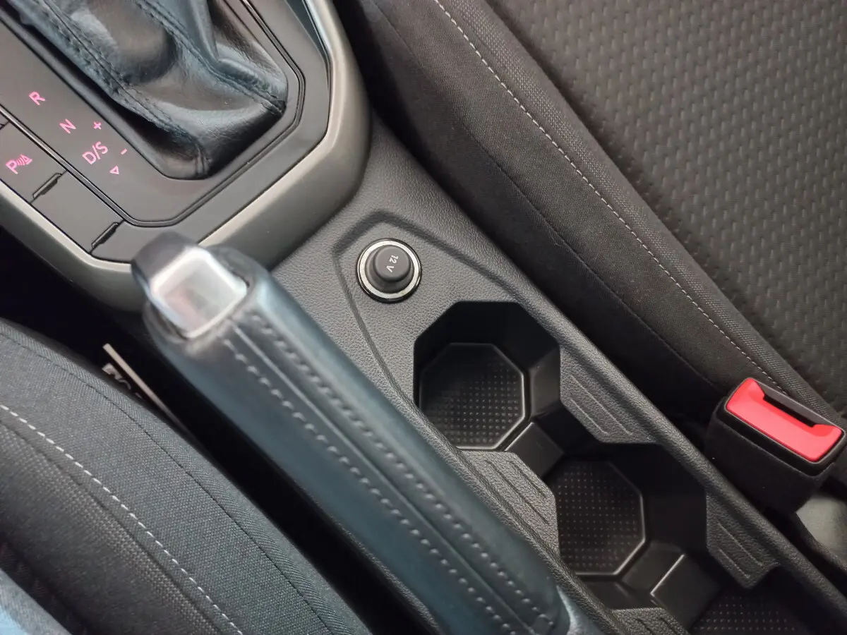 Gros plan sur la console centrale noire de la Volkswagen Polo 2020, avec frein à main, prise 12V et porte-gobelets.