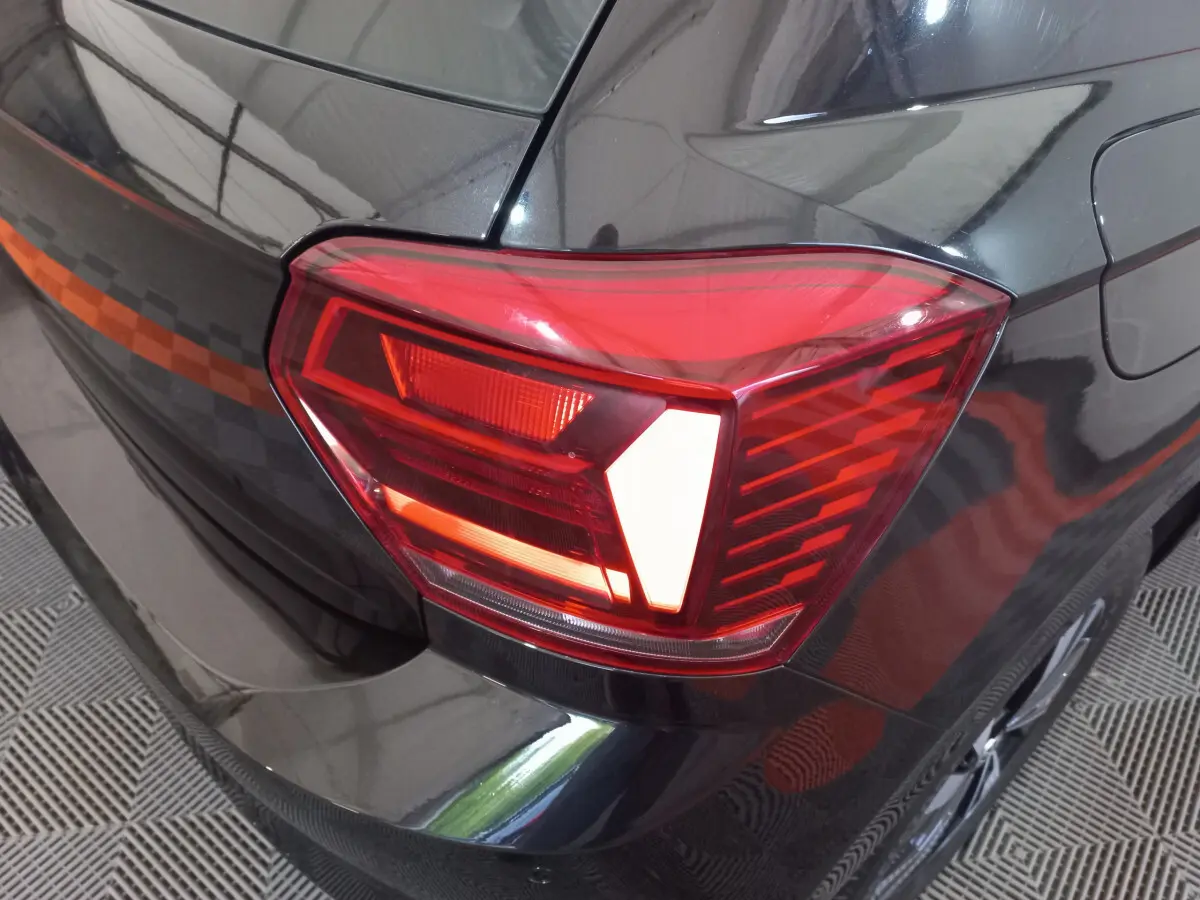 Gros plan sur le feu arrière droit rouge d'une Volkswagen Polo noire, avec une partie de la carrosserie visible.