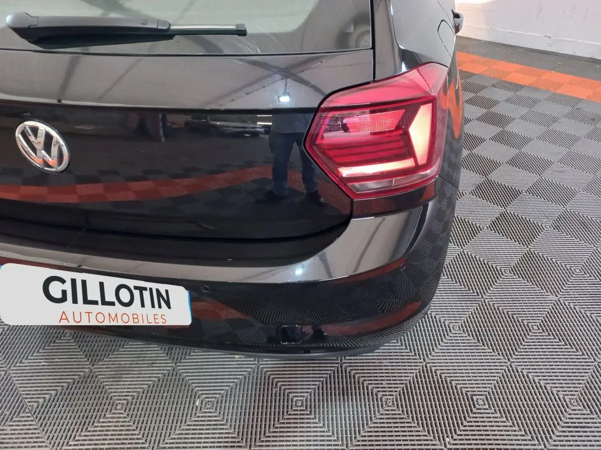 Vue rapprochée de l'arrière droit d'une Volkswagen Polo noire avec feu arrière allumé et logo VW visible.