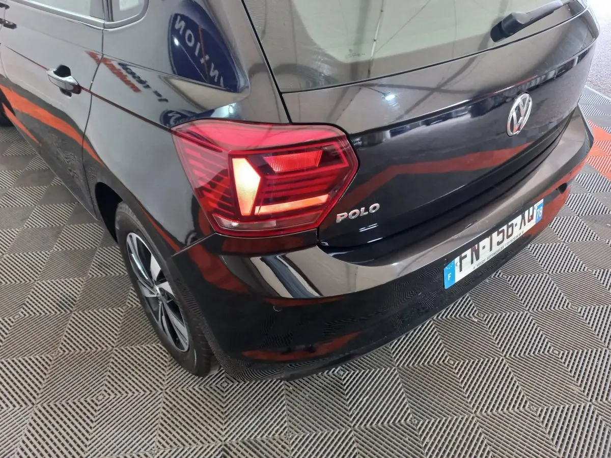 Vue 3/4 arrière gauche d'une Volkswagen Polo noire avec feux arrière allumés et logo visible sur hayon.