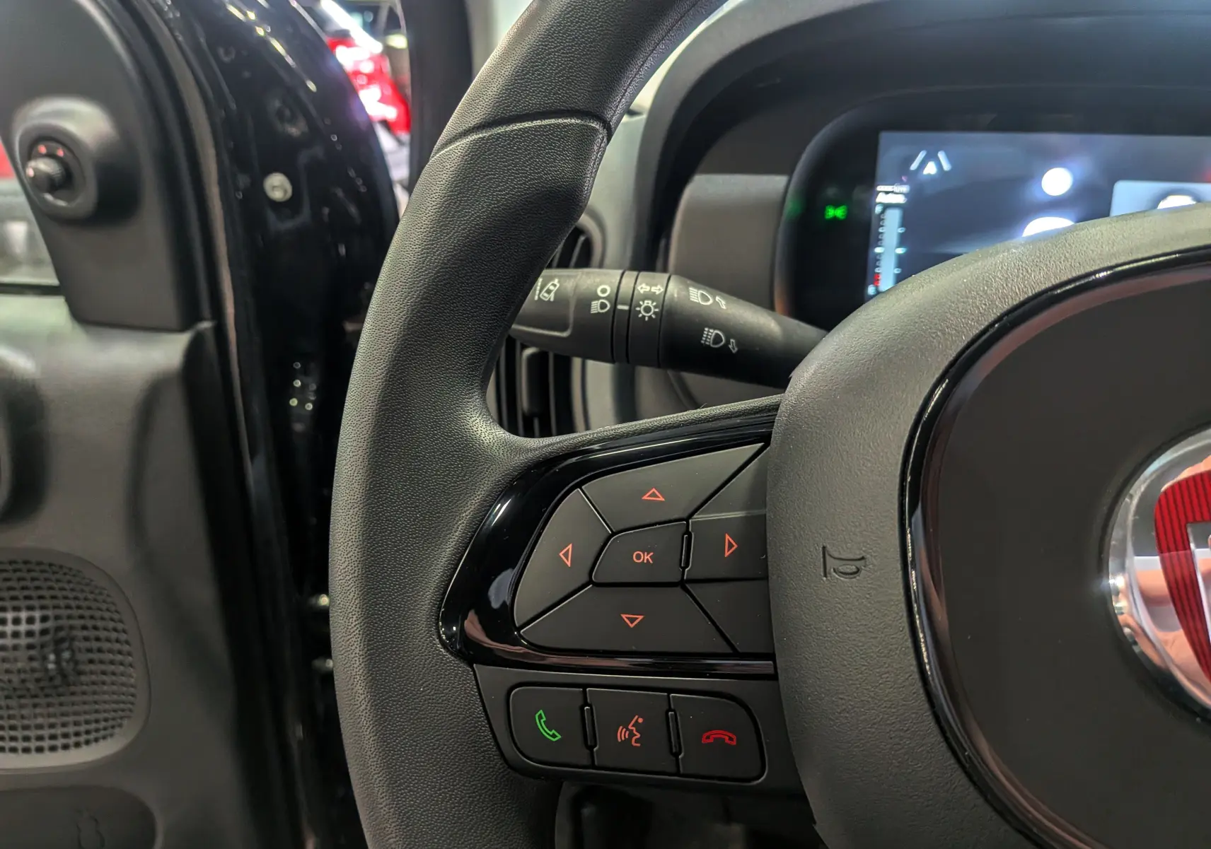 Gros plan sur le volant noir de la Fiat Panda 2025 hybride avec commandes intégrées et tableau de bord numérique partiel.