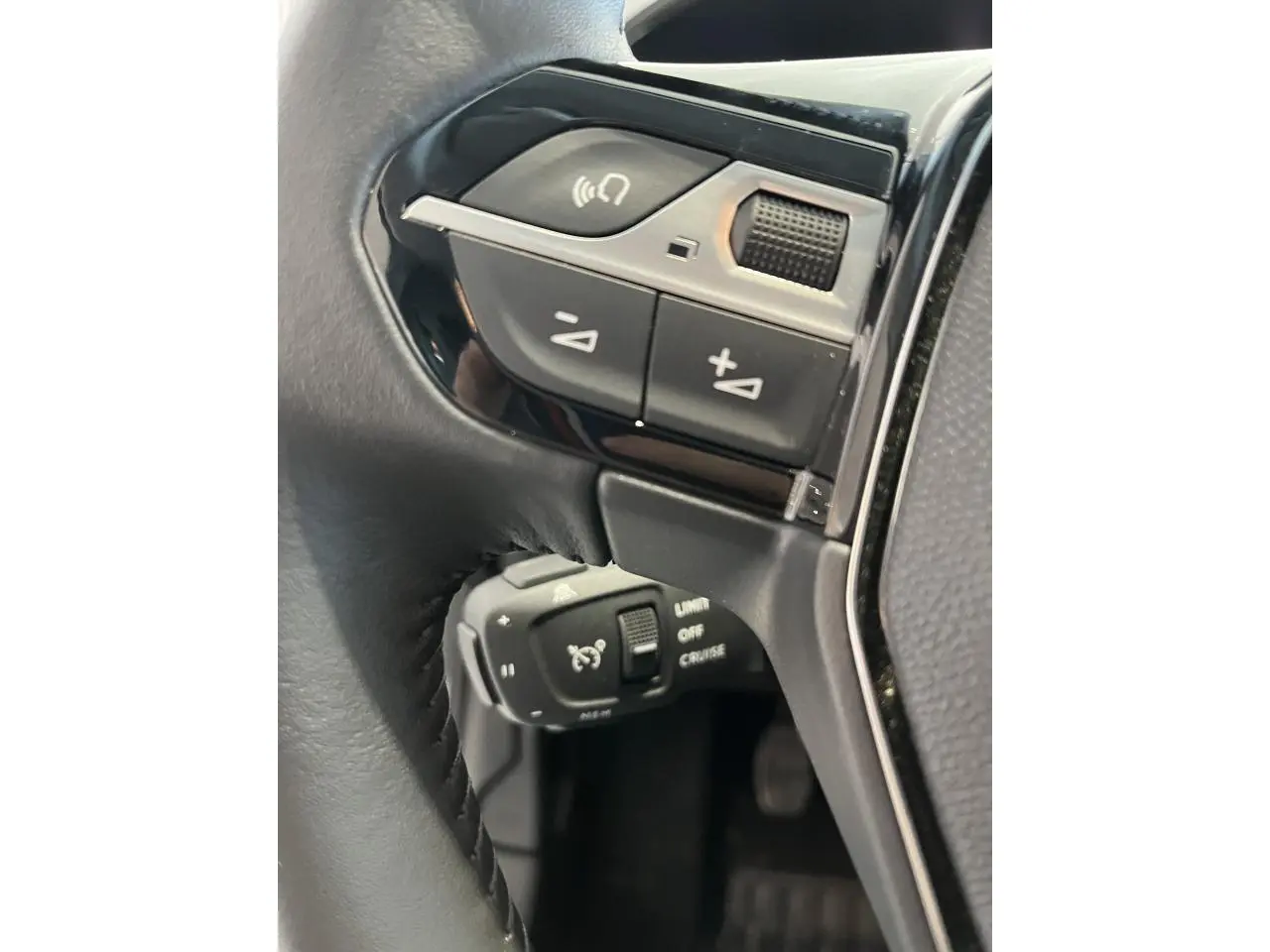 Gros plan sur les commandes multifonctions et régulateur de vitesse au volant cuir noir de la Peugeot 208 gris clair.