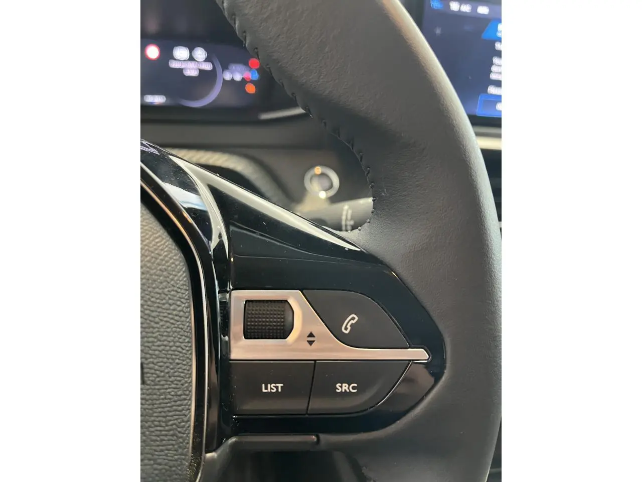 Gros plan sur les commandes multimédia à gauche du volant cuir d'une Peugeot 208 gris clair Selenium 2024.