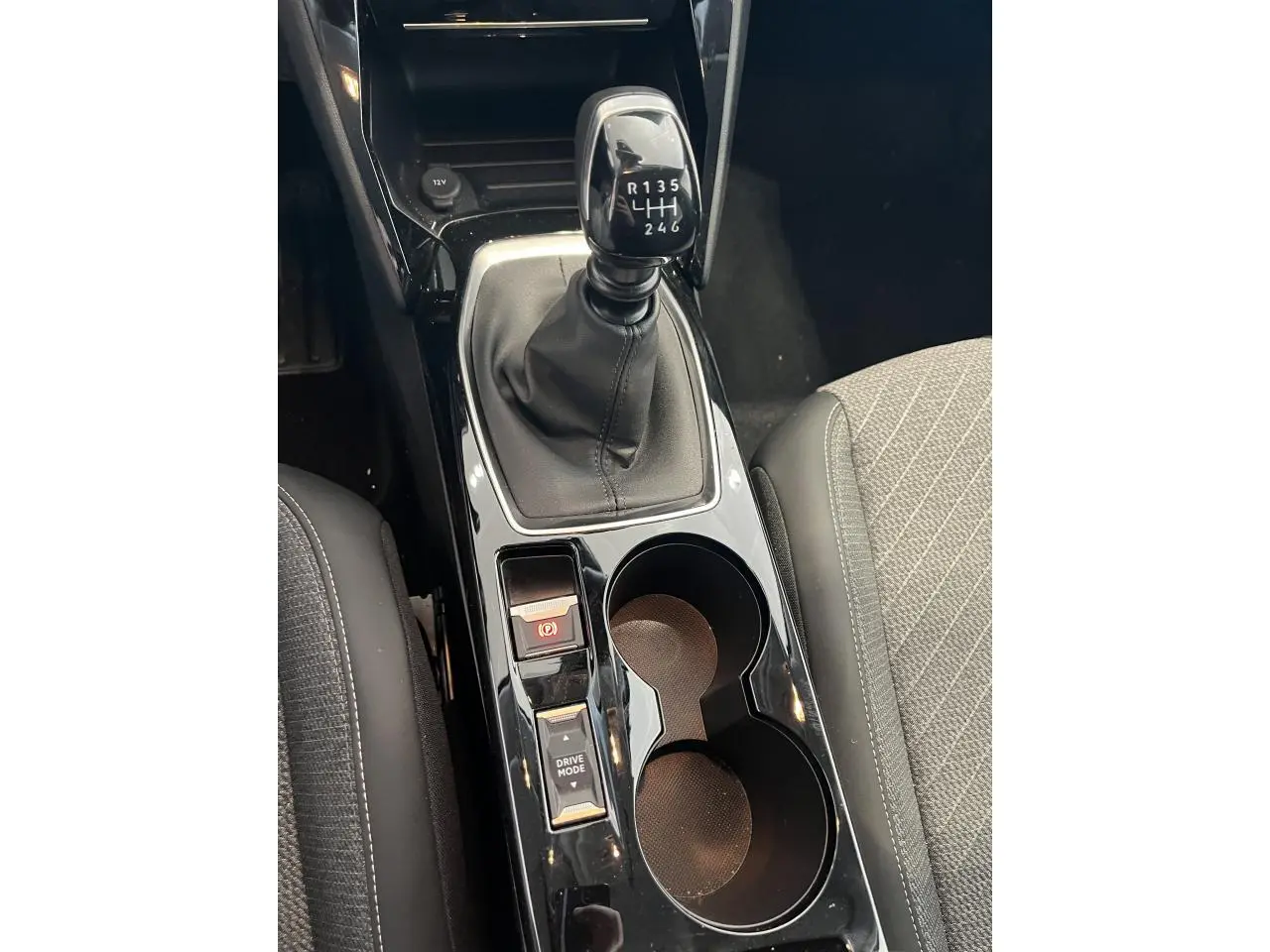 Vue rapprochée de la console centrale noire brillante avec levier de vitesses manuelle et porte-gobelets sur Peugeot 208 gris clair Selenium.
