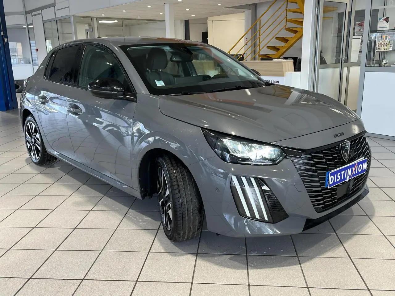 Peugeot 208 gris clair sélénium vue 3/4 avant droit avec calandre noire et feux LED 3 griffes allumés.