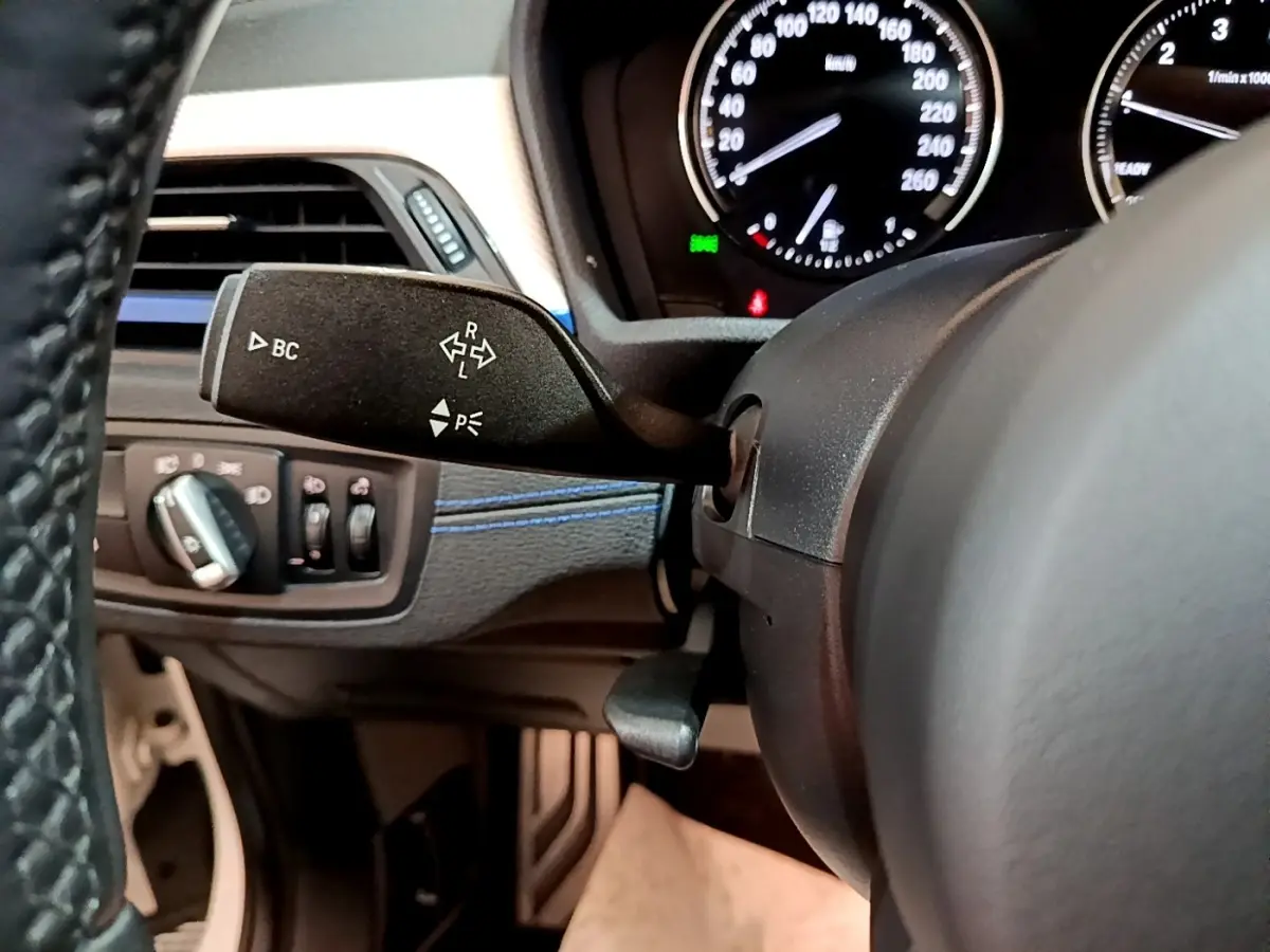 Gros plan sur le commodo gauche et le tableau de bord noir avec compteurs blancs du BMW X1 sDrive18i M Sport 2022.